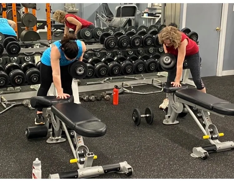 Three members doing single-arm dumbbell rows on benches beside the dumbbell rack.