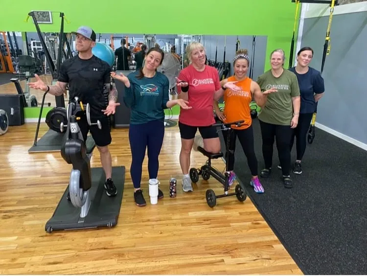 Six members joking around in the training room in front of the green accent wall.