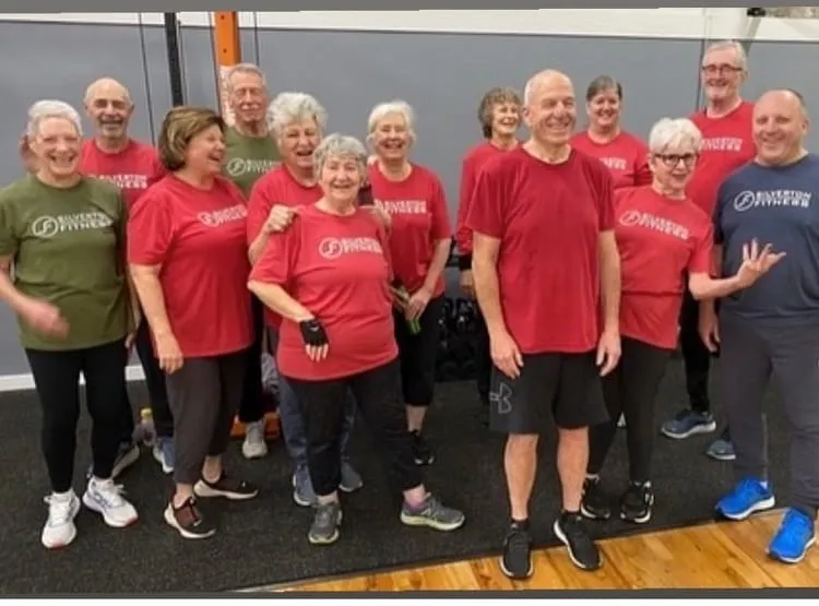Thirteen members in Silverton Fitness team shirts, laughing together on the training floor.