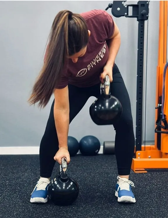 A member in a Silverton Fitness shirt doing a bent-over row with two kettlebells.