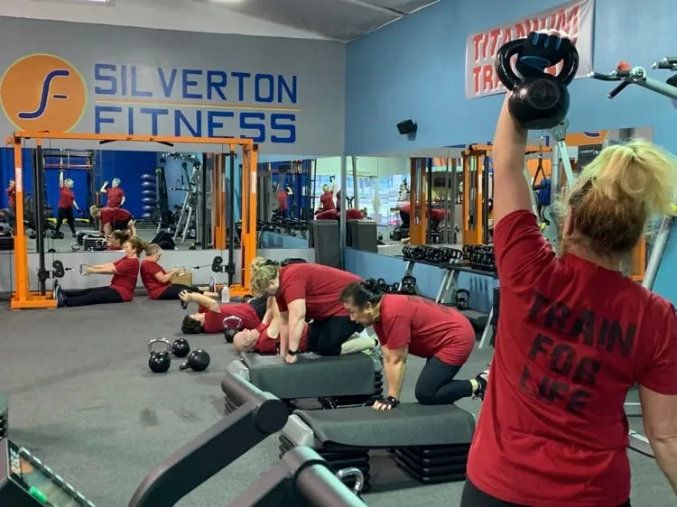 A Team Training session under the Silverton Fitness wall logo — one member pressing a kettlebell overhead while others work behind her.